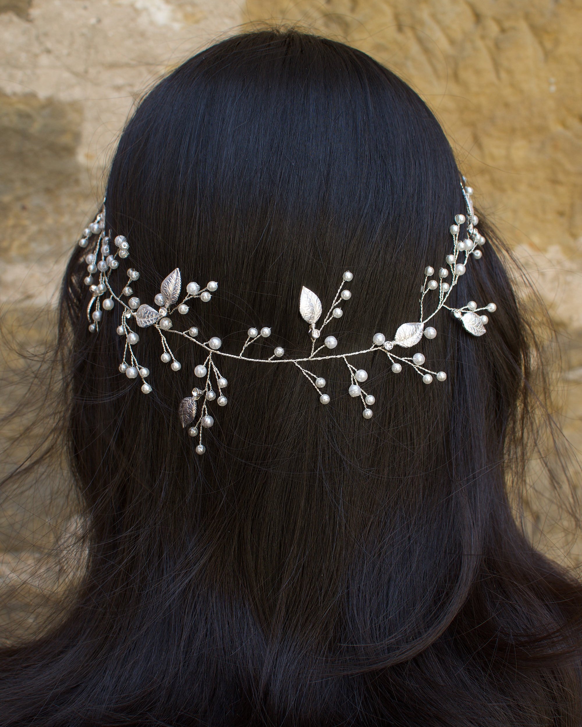 A silver pearl bridal vine with leaves worn by a dark haired model on the back of her head