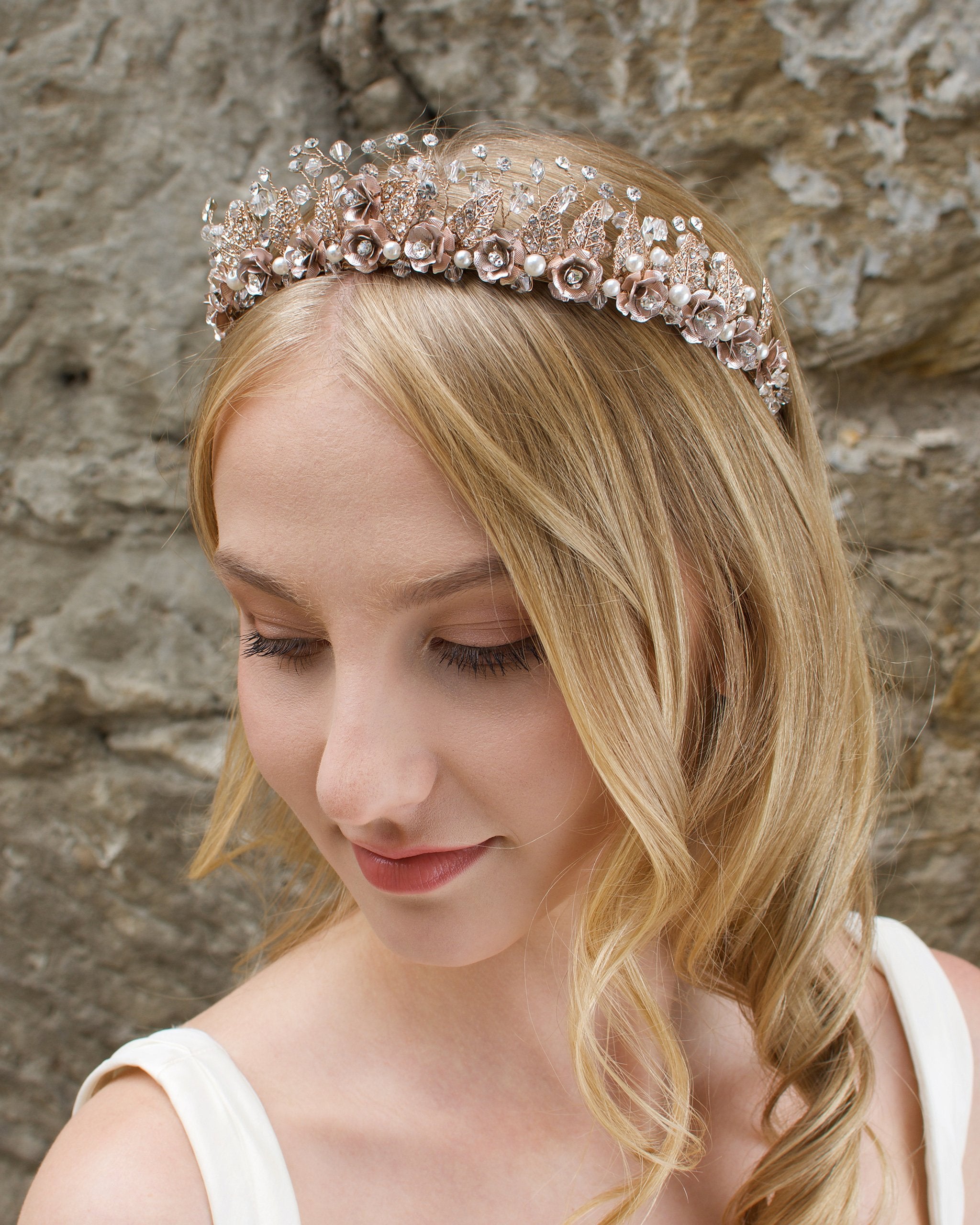 A Rose Gold Flowers and pearls wide tiara worn by a blonde bride with a stone wall background.