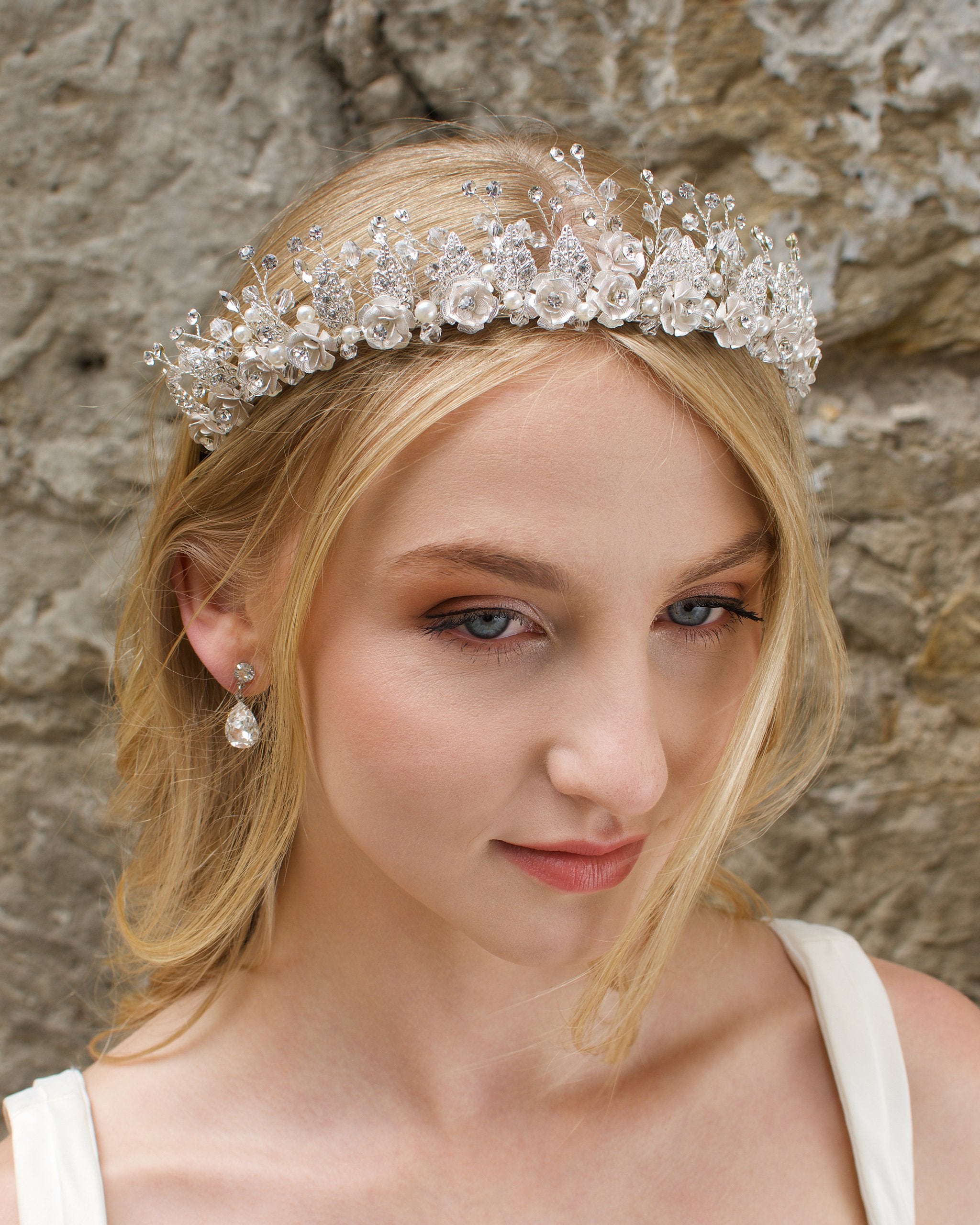 A Silver Flowers and pearls wide tiara worn by a blonde bride with a stone wall background.