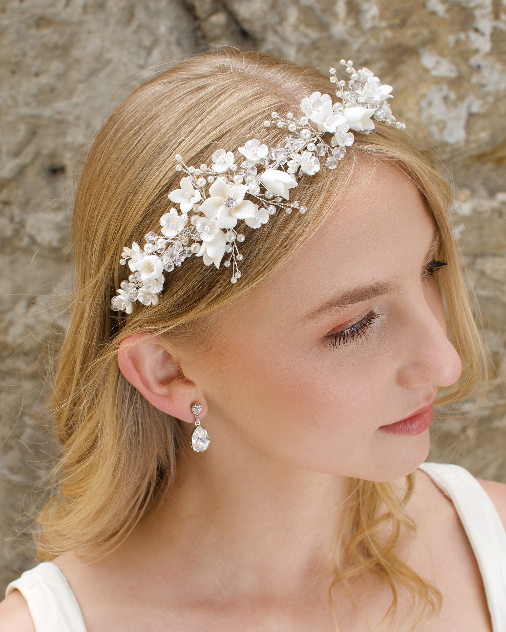 A blonde Bride wears a headband of ceramic flowers and pearls with a stone wall background