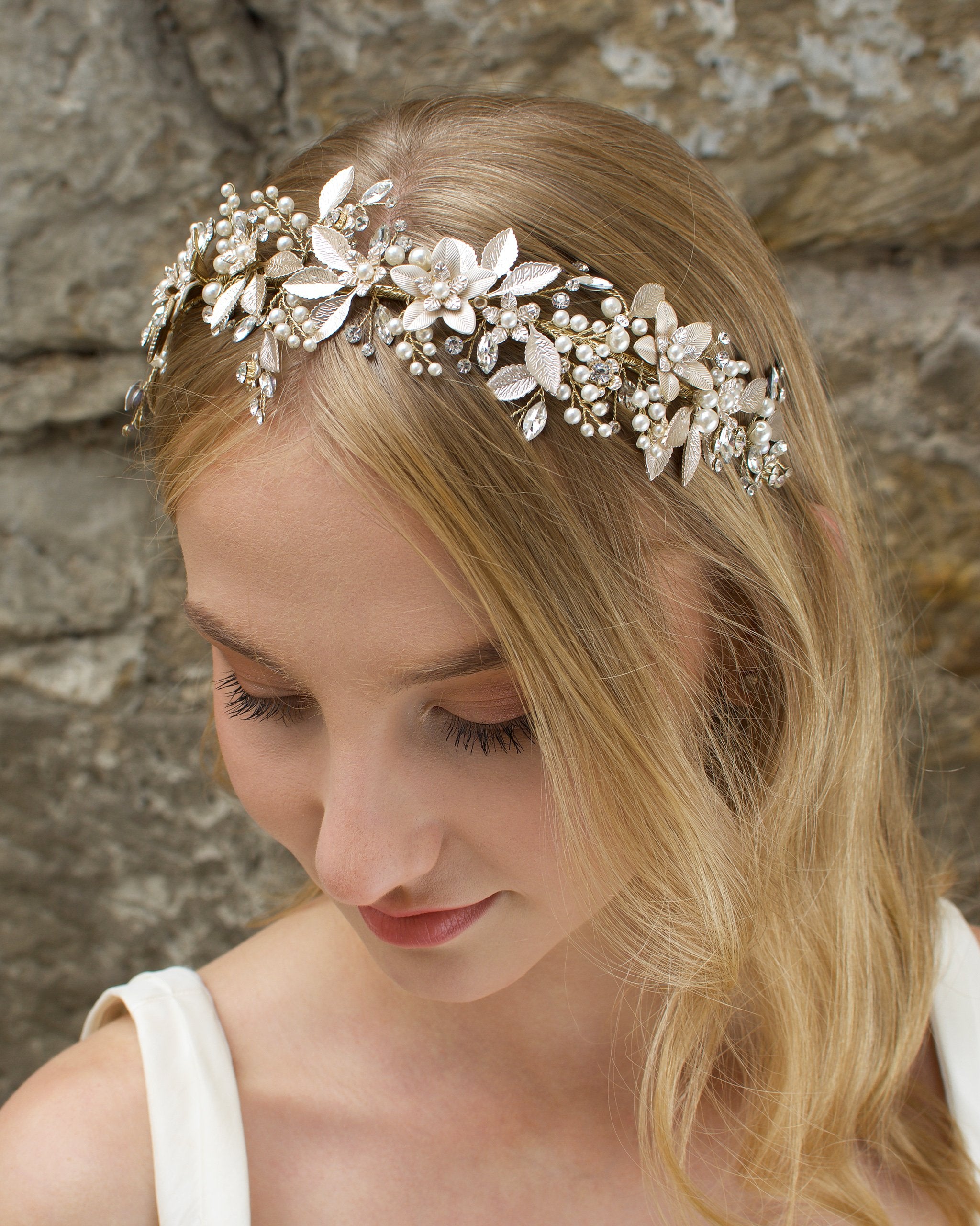 Blonde model wears a very pale gold bridal headband with a stone wall background