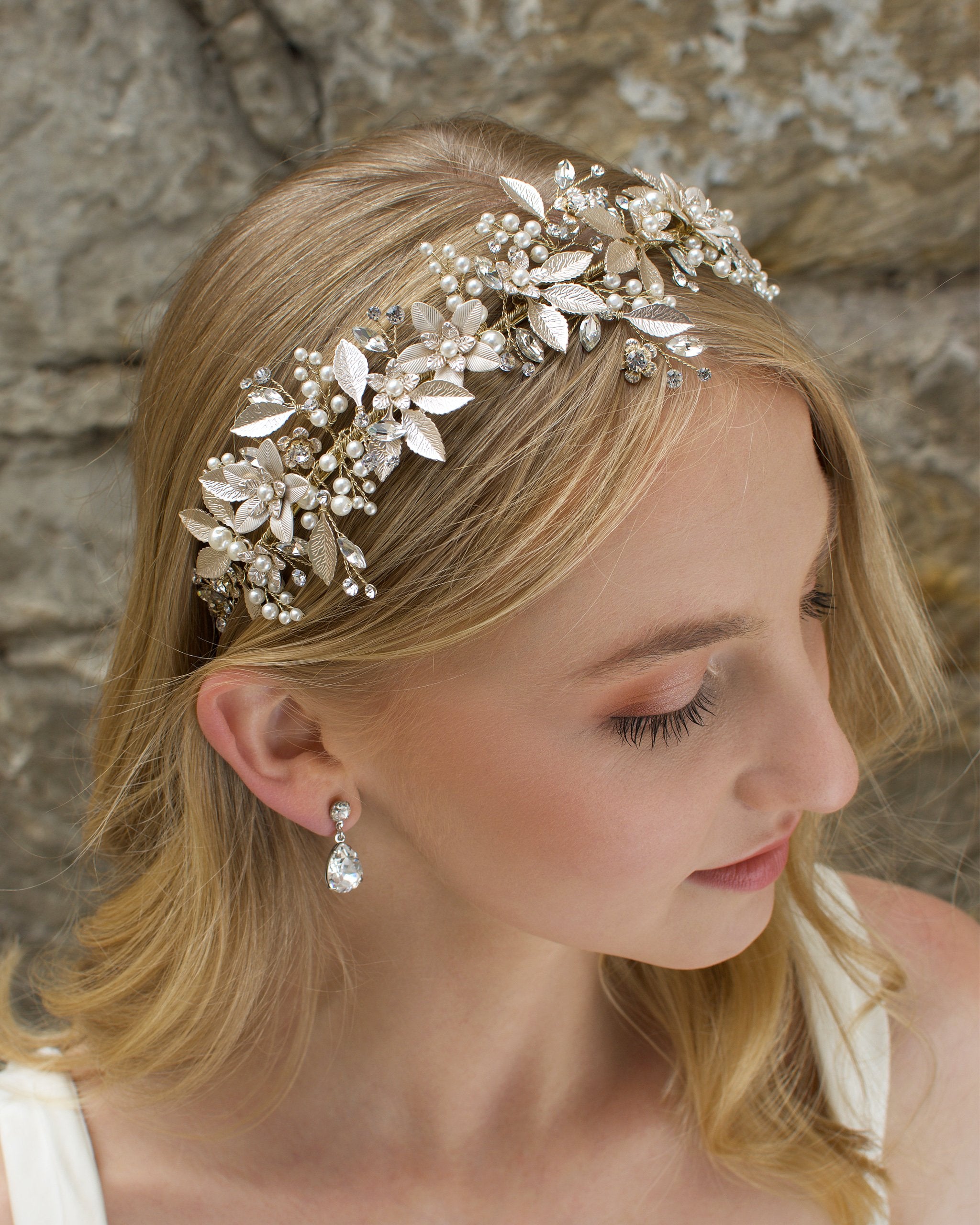 Blonde hair Bride wears a Champagne Gold wide bridal headband with leaves with a stone wall background
