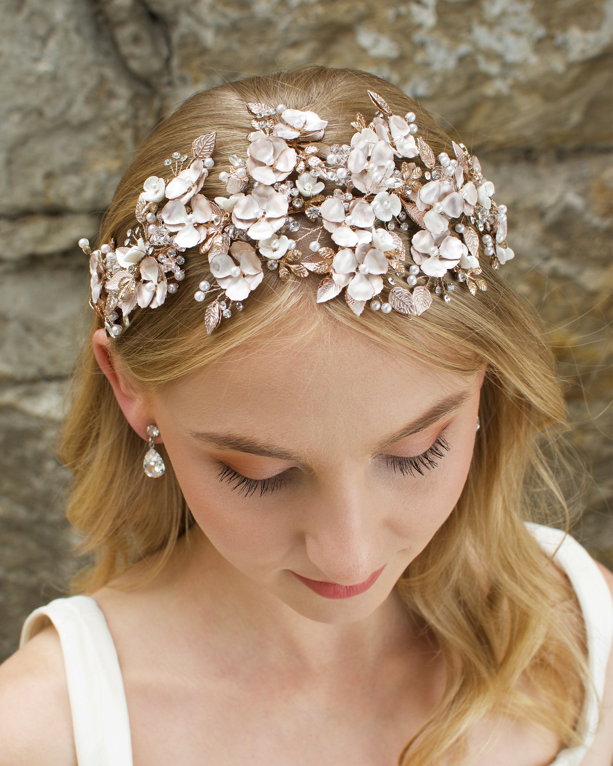 Blonde Haired model wears a wide headband of flowers with the background of a stone wall