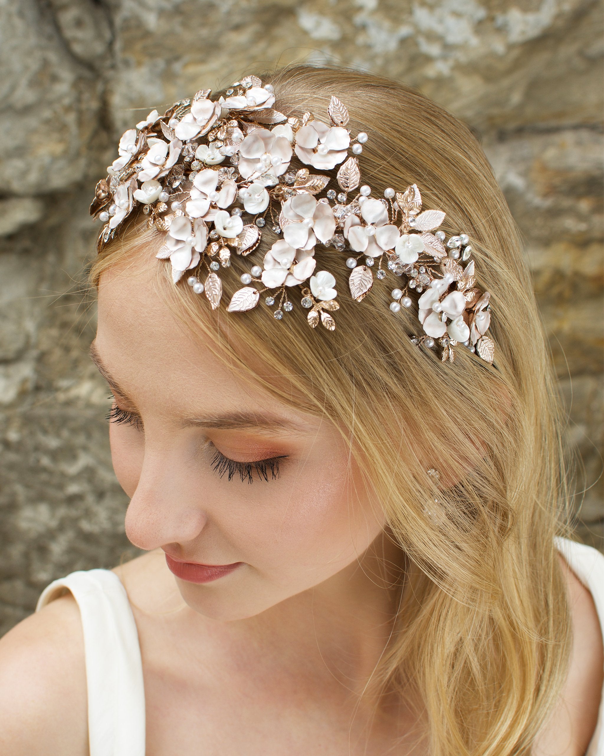 Blonde model wears a wide headband of flowers with the background of a stone wall