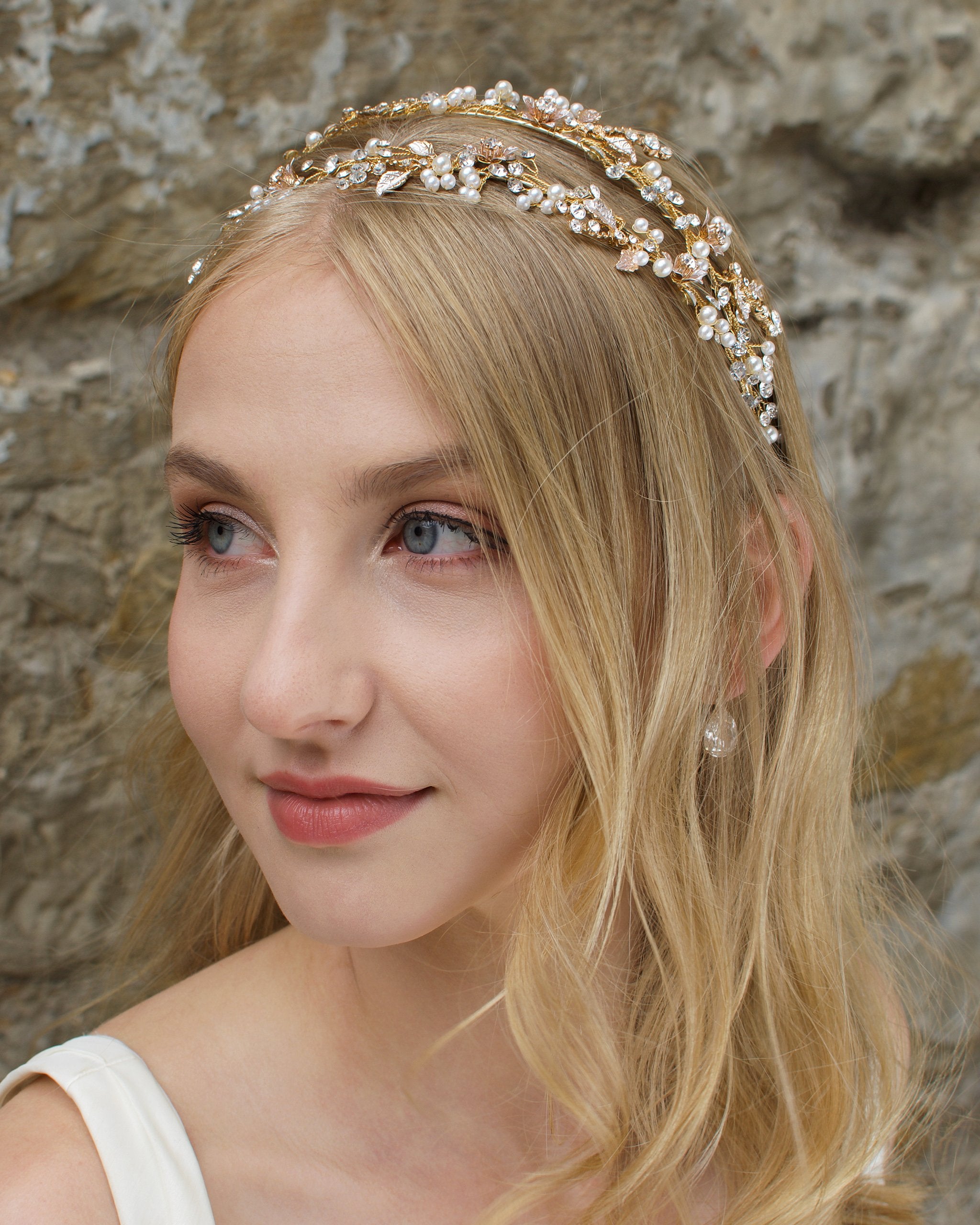 Blonde Bride with green eyes wears a double row bridal headband in gold with a stone wall background