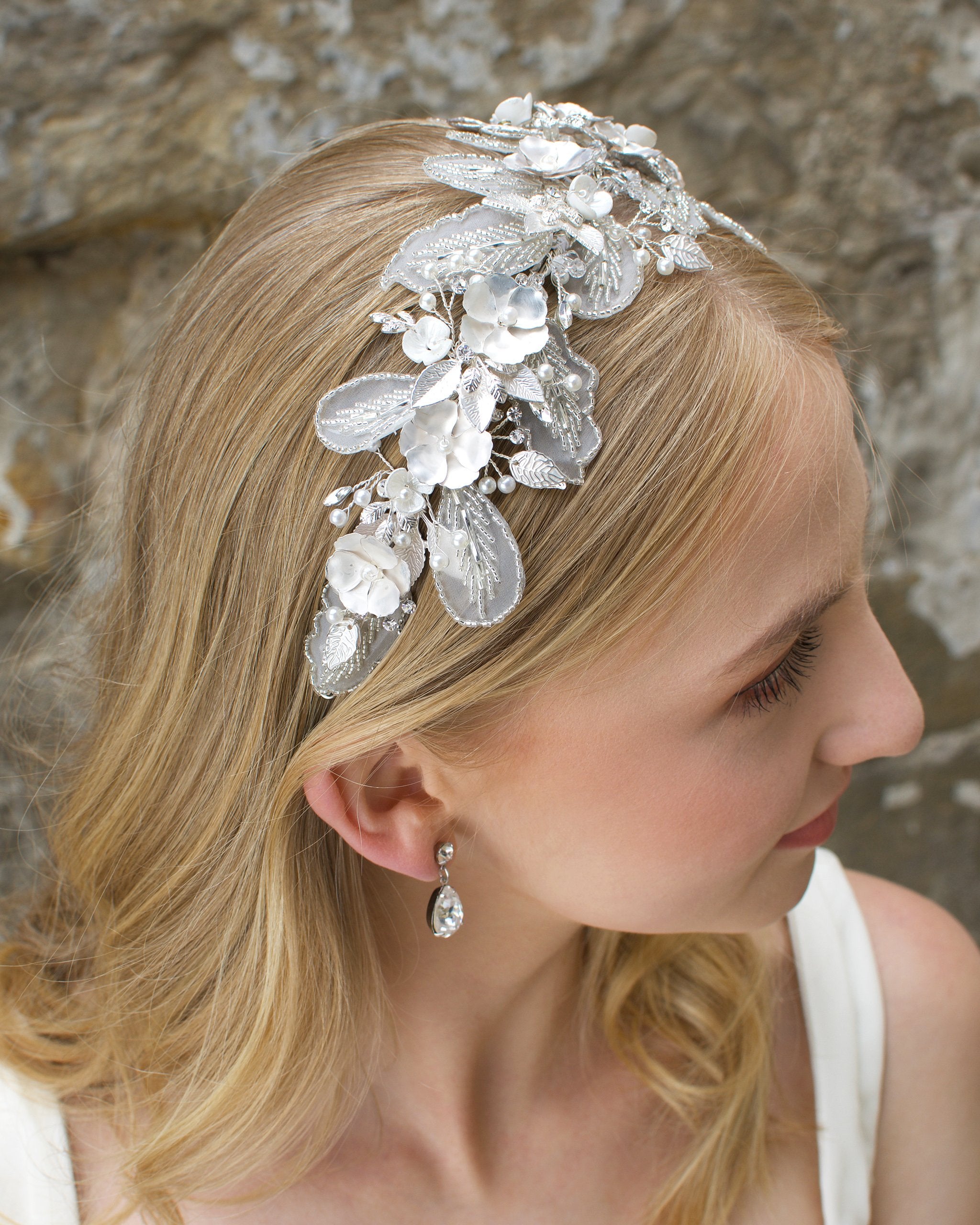 Bridal headband with Lace leaves and white flowers worn by a blonde bride in front of a stone wall.
