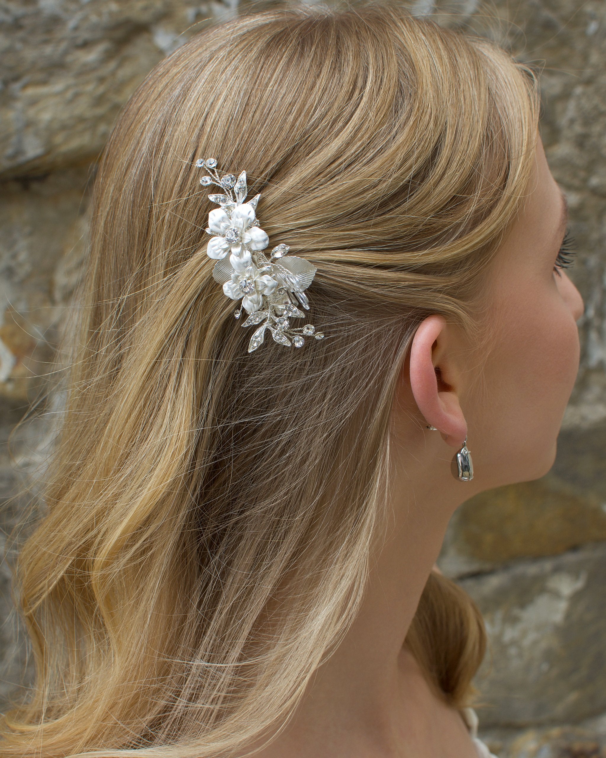 Blonde model wears a small silver flower clip in front of a stone wall