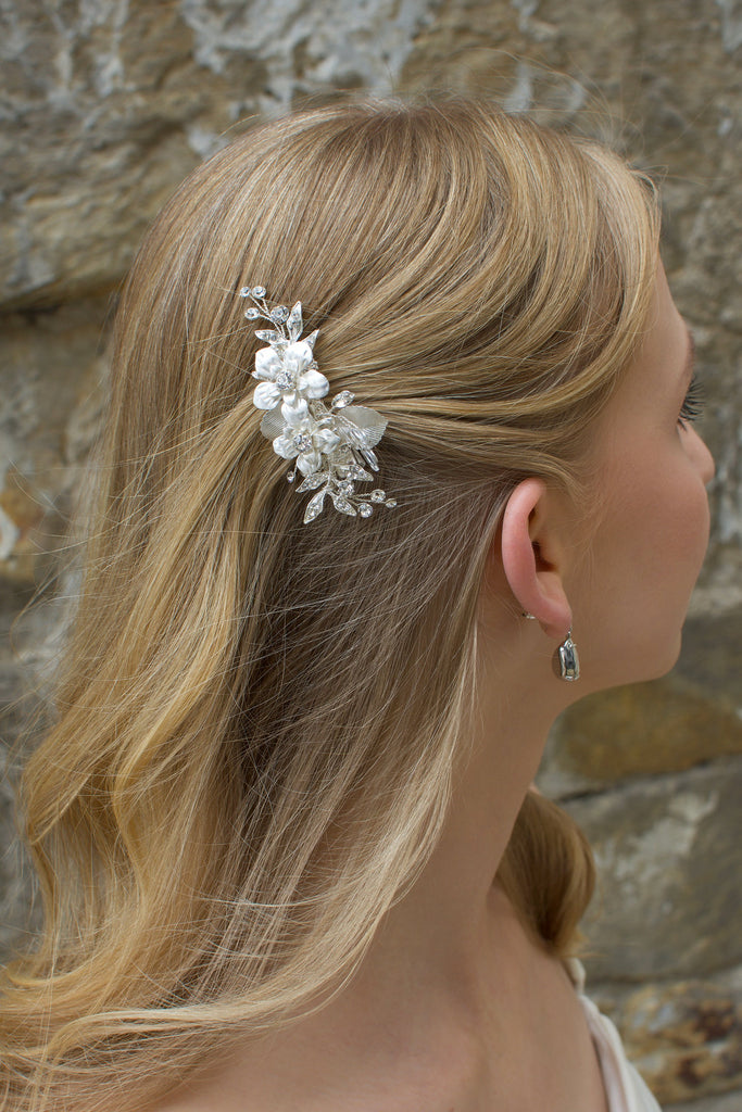 Blonde model wears a small silver flower clip in front of a stone wall