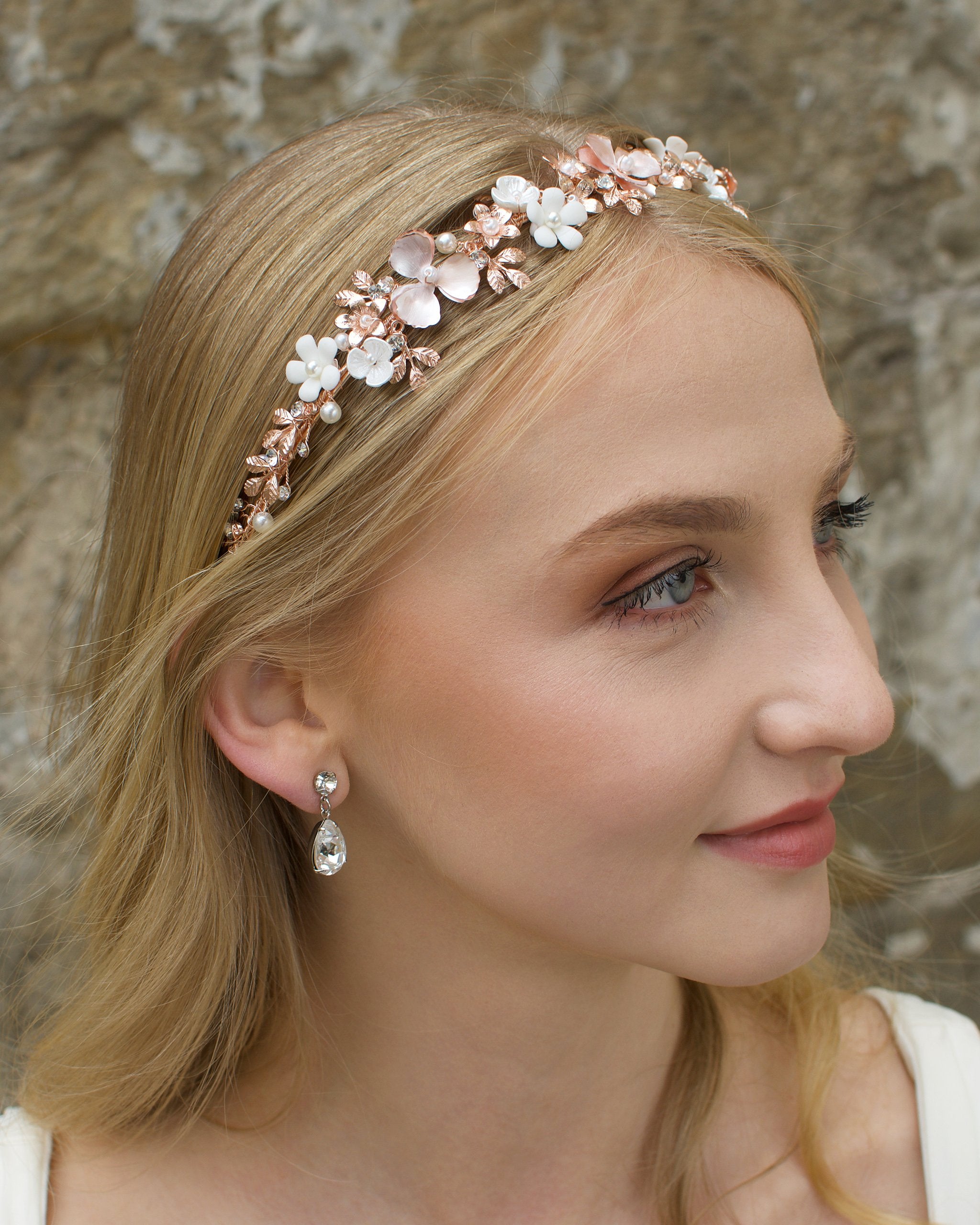 Blonde Bride wearing a pale Rose Gold headband with flowers with a stone background