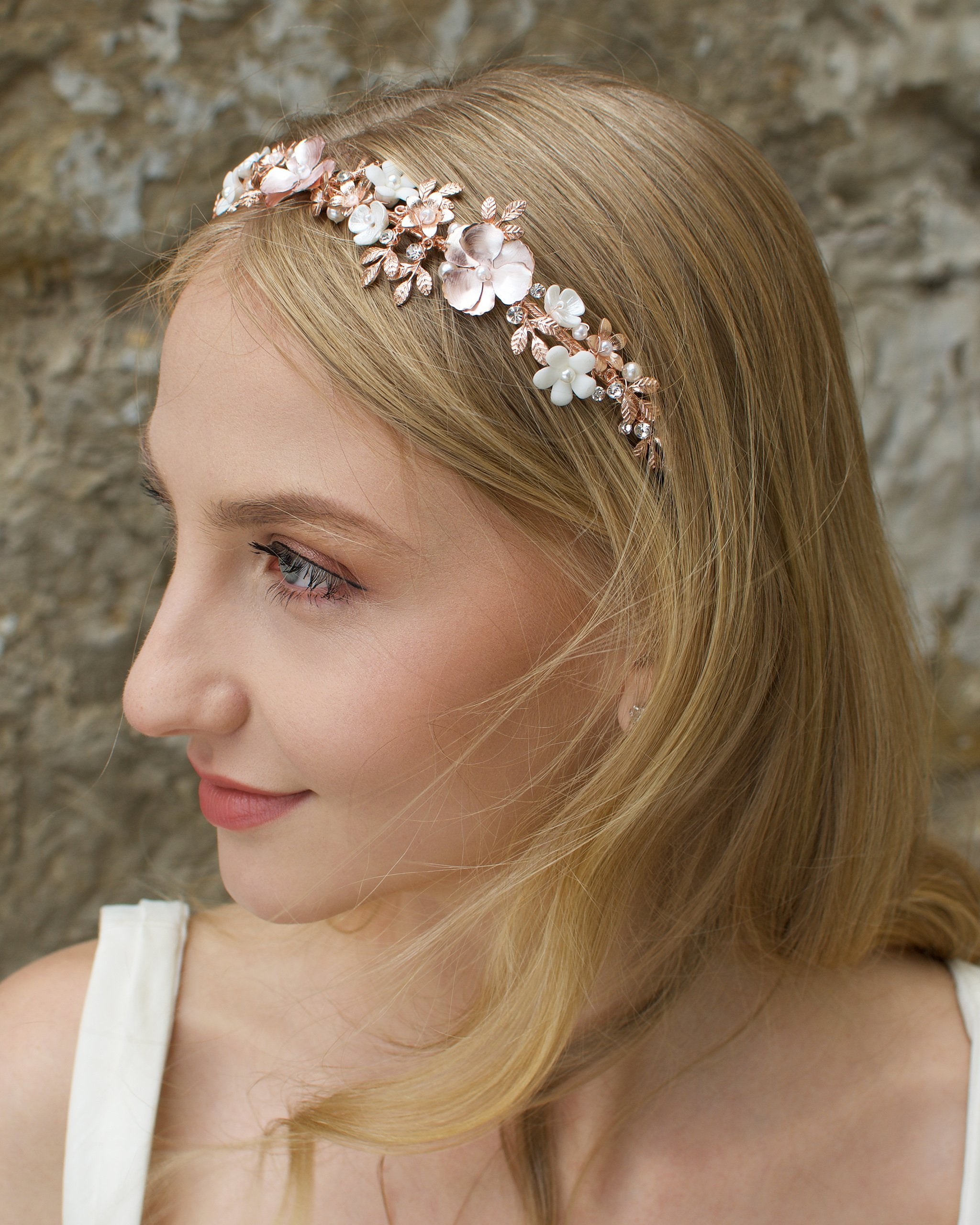 Blonde haired Bridal model wearing a pale rose gold bridal headband with stone background