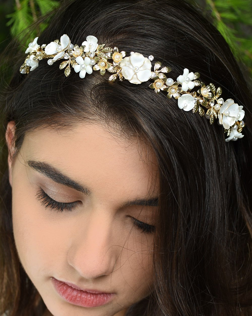 White Flowers and gold leaves headband worn at the front of a dark hair model's head with pine tree background