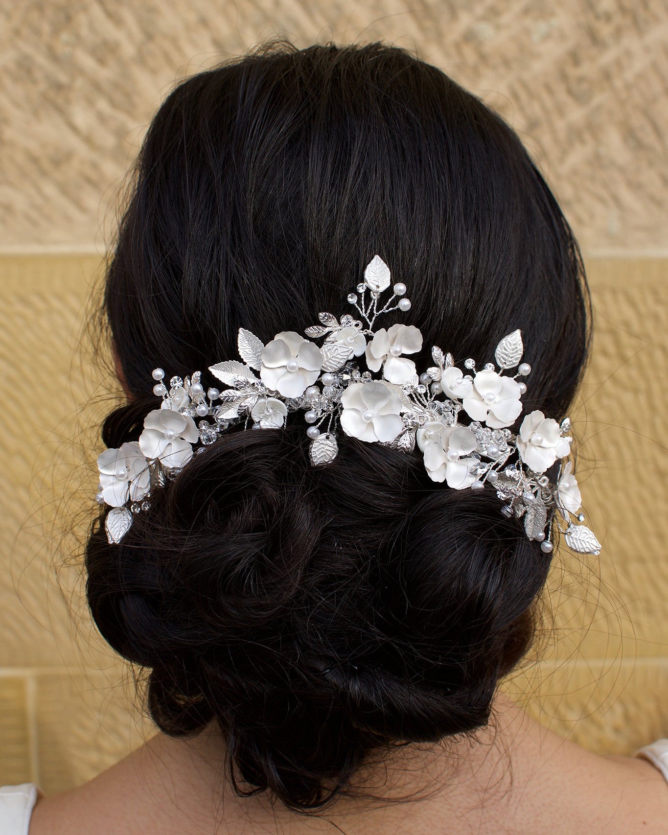 Silver flowers and leaves bridal hair piece with a white look worn by a curly haired model with a stone wall background.