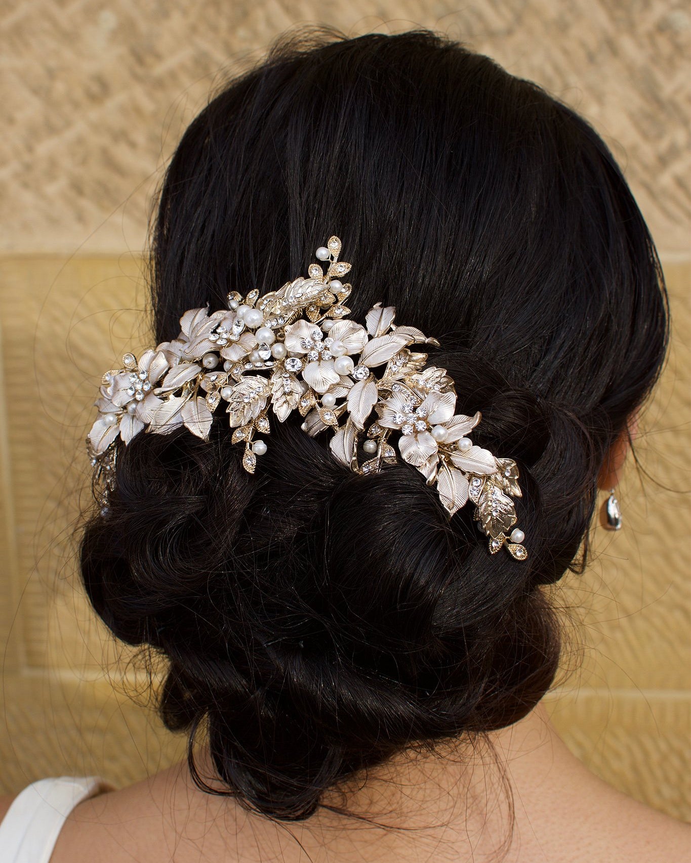 A wide Bridal Headpiece of gold leaves at the back of a model's head with a stone wall backdrop