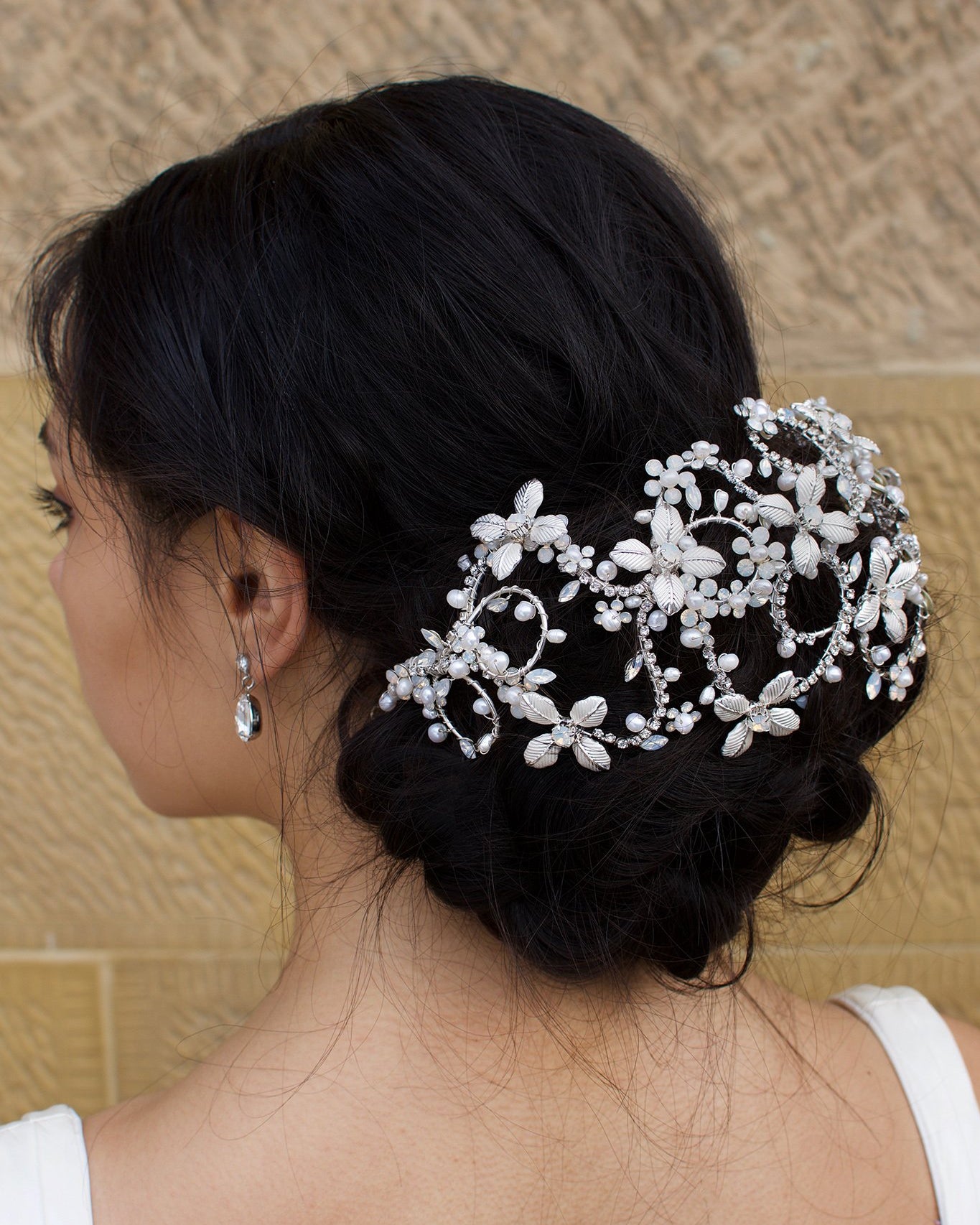 Dark hair model wears a Silver Bridal Headpiece over a large bun of hair with a stone wall background
