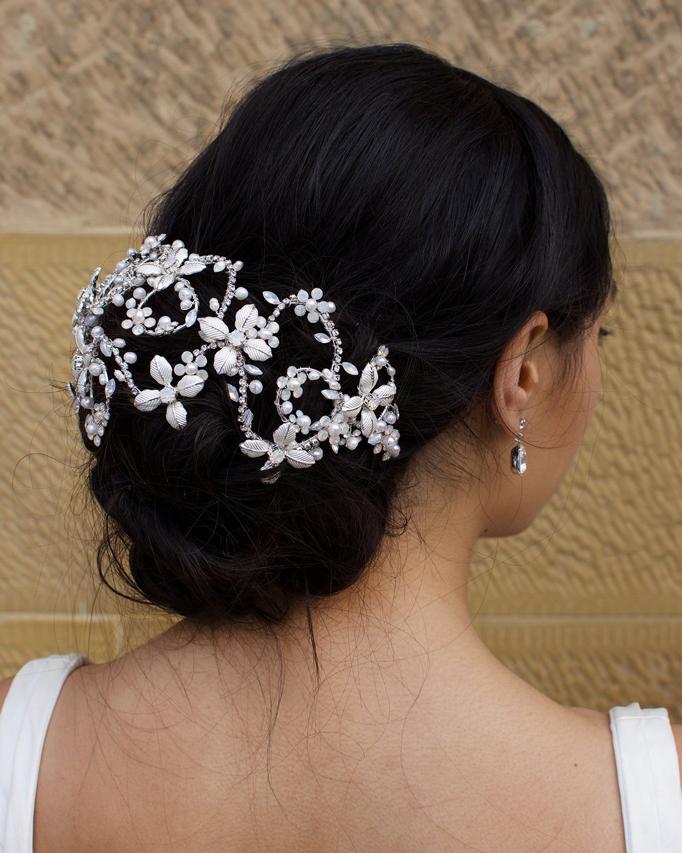 Looking right a Bridal Model wears a silver wide headband on her dark hair with a stone wall background