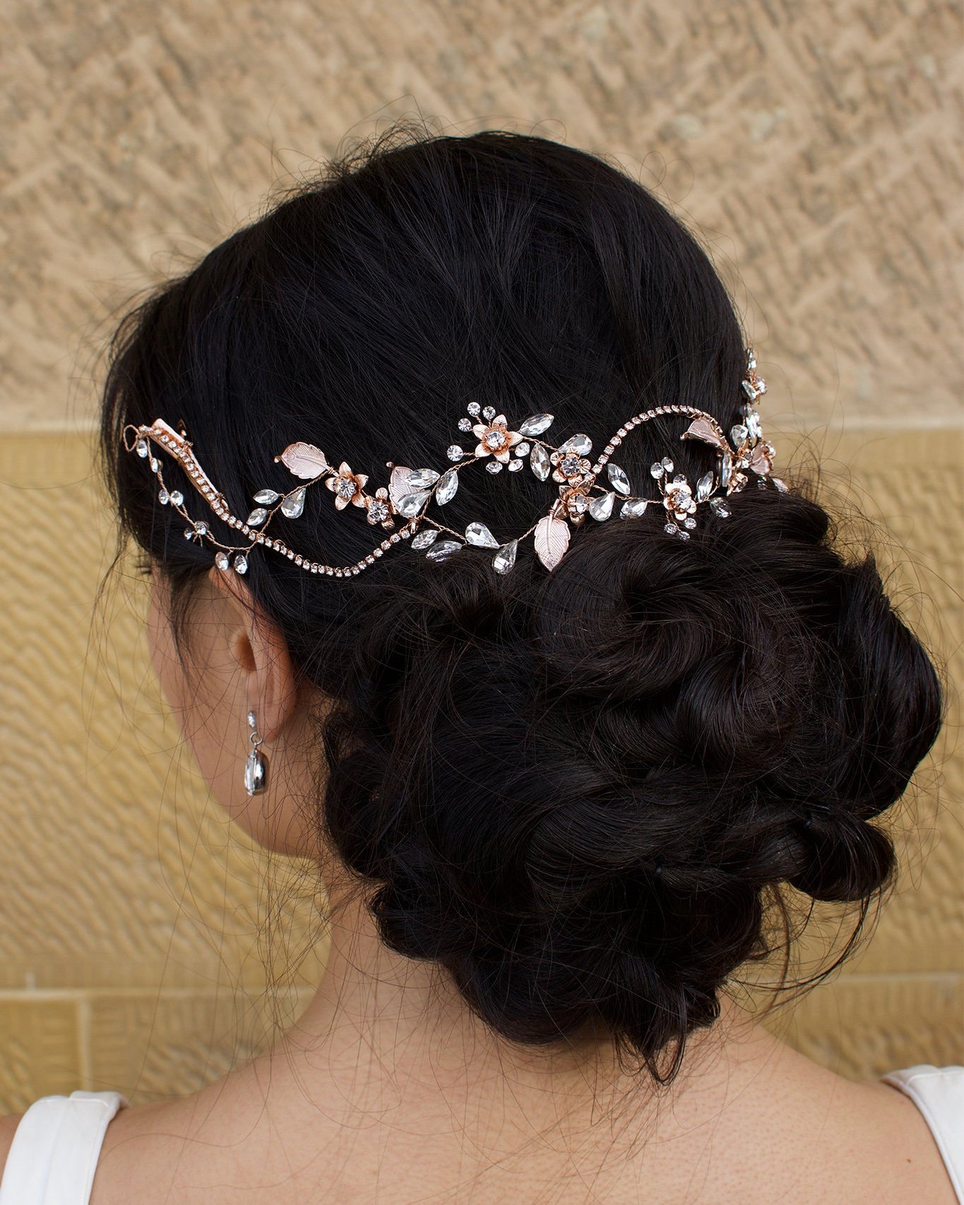 Weaving rows of Rose Gold Hair Vine across the back of a models dark hair with a stone background