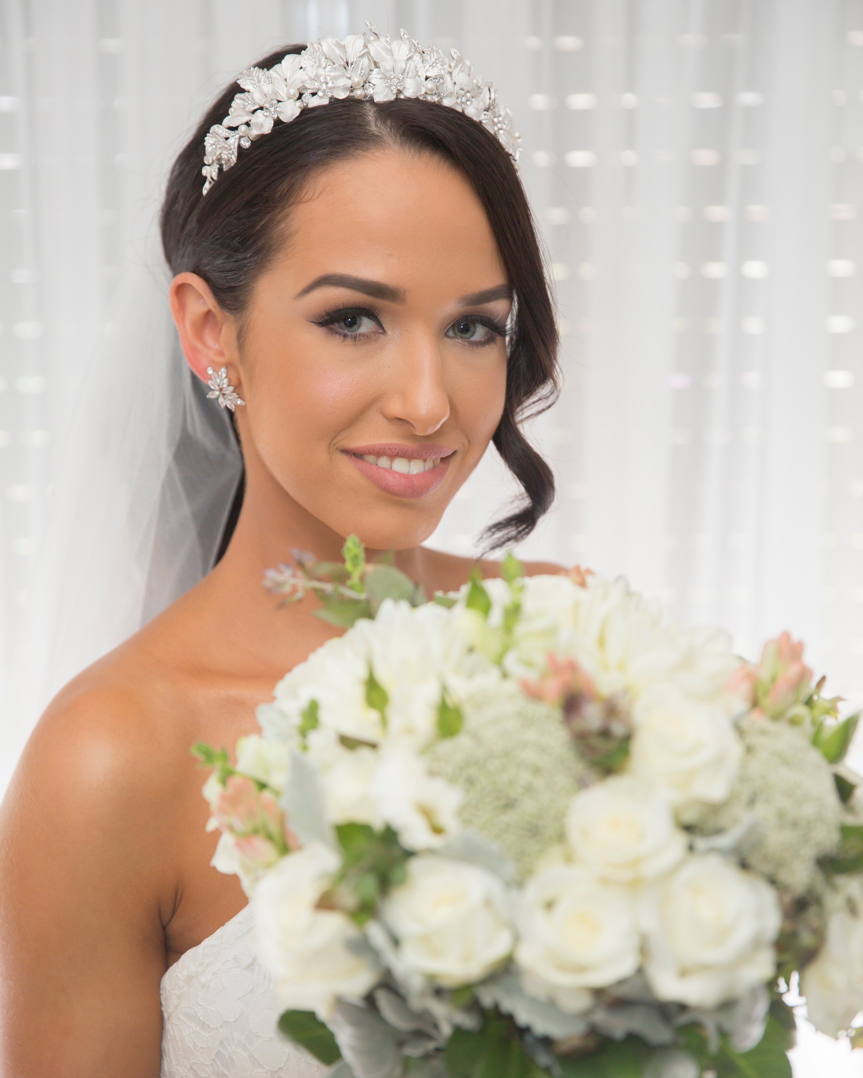 Bride with bouquet of flowers wearing a silver leaf crown and a curl of hair down one side