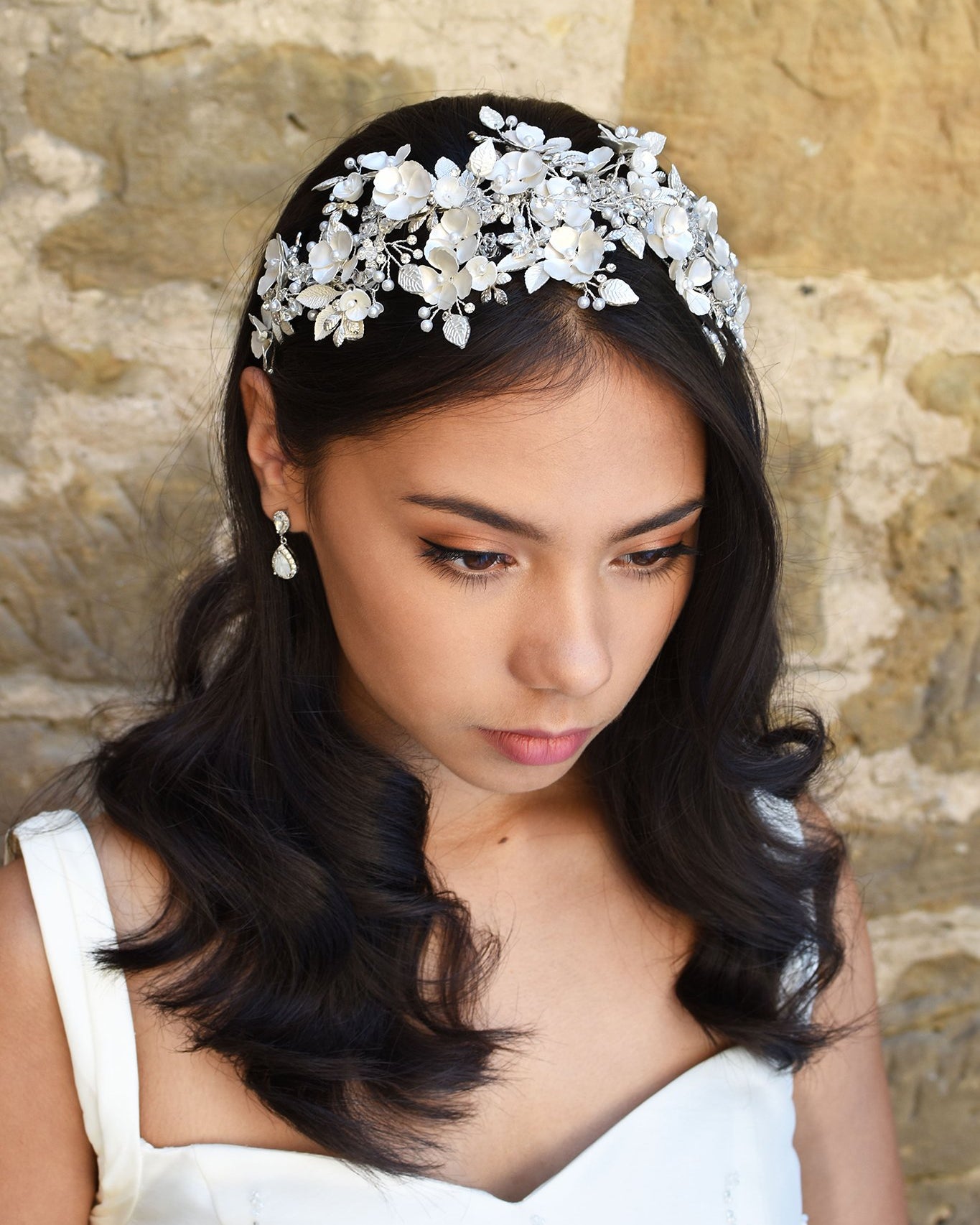 Dark Haired model wears a wide headband of flowers with the background of a stone wall