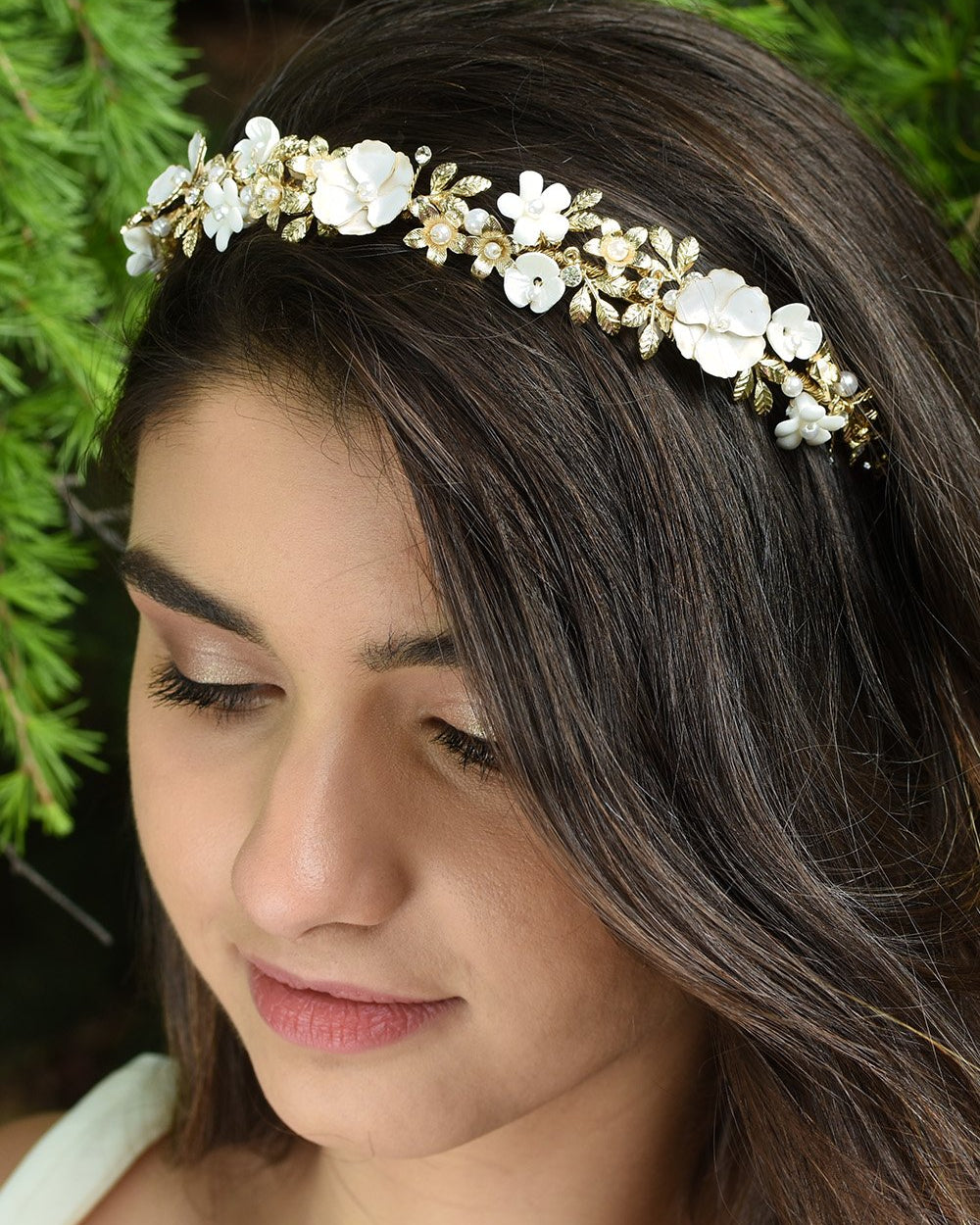 Smiling Dark hair Bridal Model wearing Flower and gold headband with green pine tree background