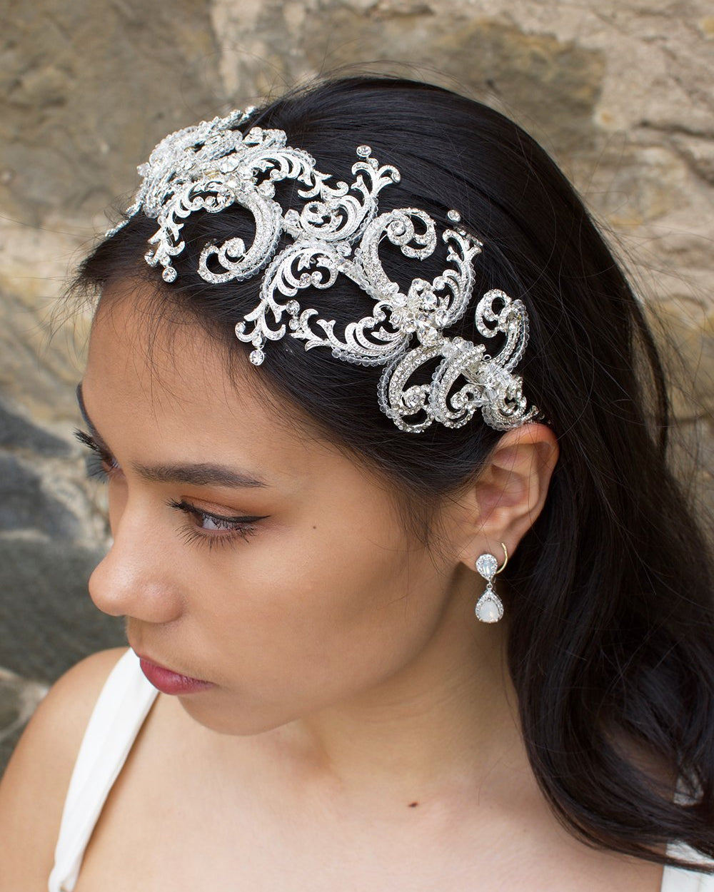 Wide Silver and clear crystal bridal headband worn by a dark haired bride with a stone backdrop