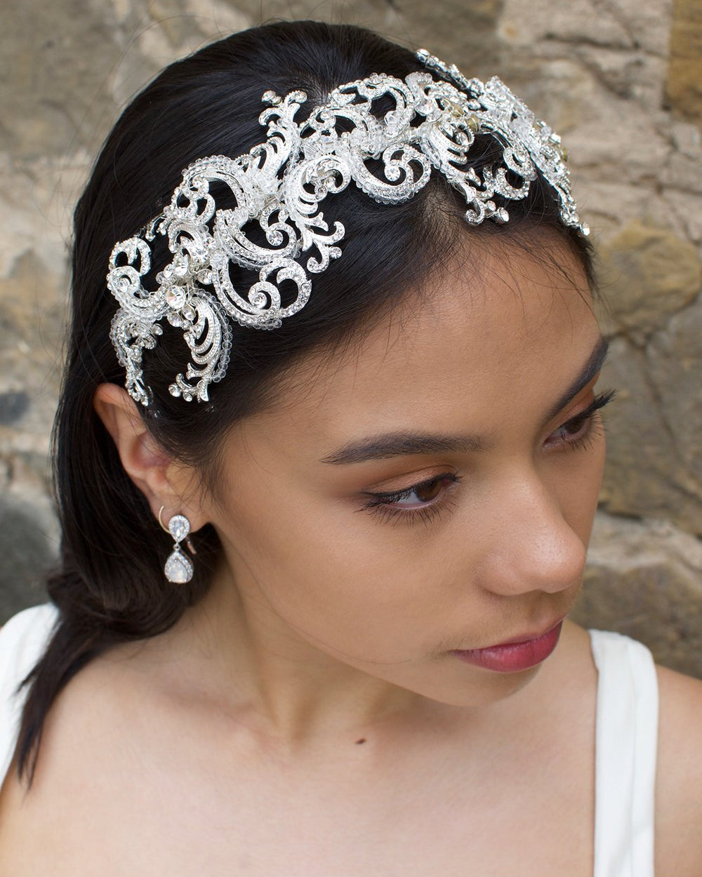 Wide swirling Bridal Headband in Silver with clear crystals worn by a dark haired model with a stone wall backdrop