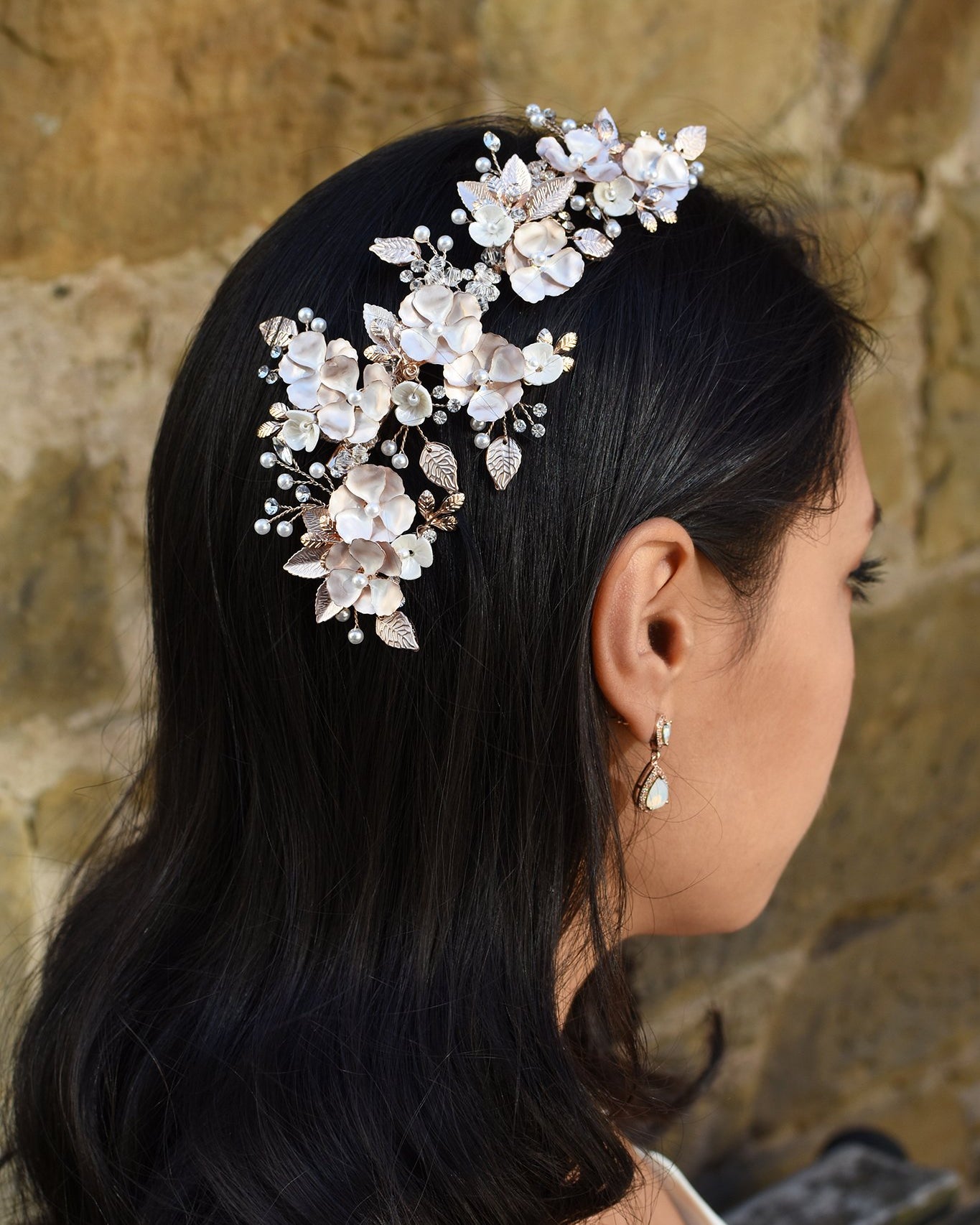 A Dark haired model wears a long Pale gold side comb with flowers and a small earring