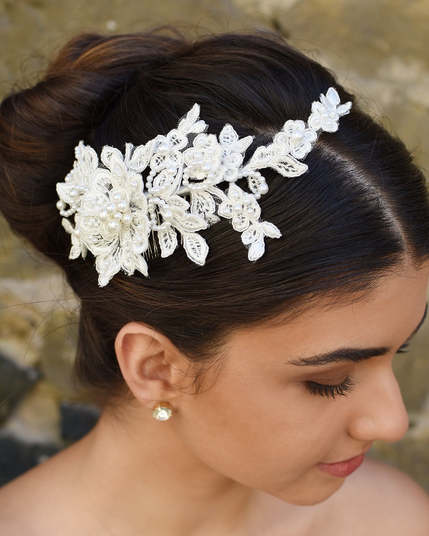 Lace side comb with pearls worn by a dark hair model in front of a stone wall.
