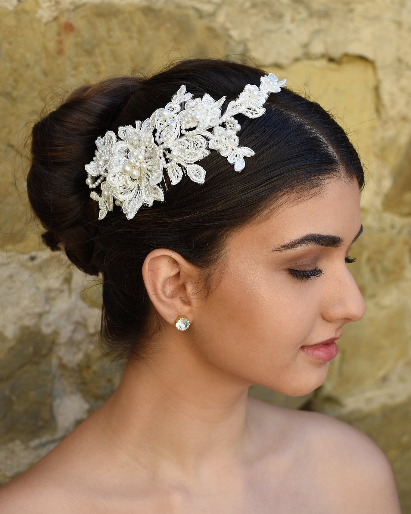 Delicate Lace side comb with pearls worn by a bride in front of a stone wall