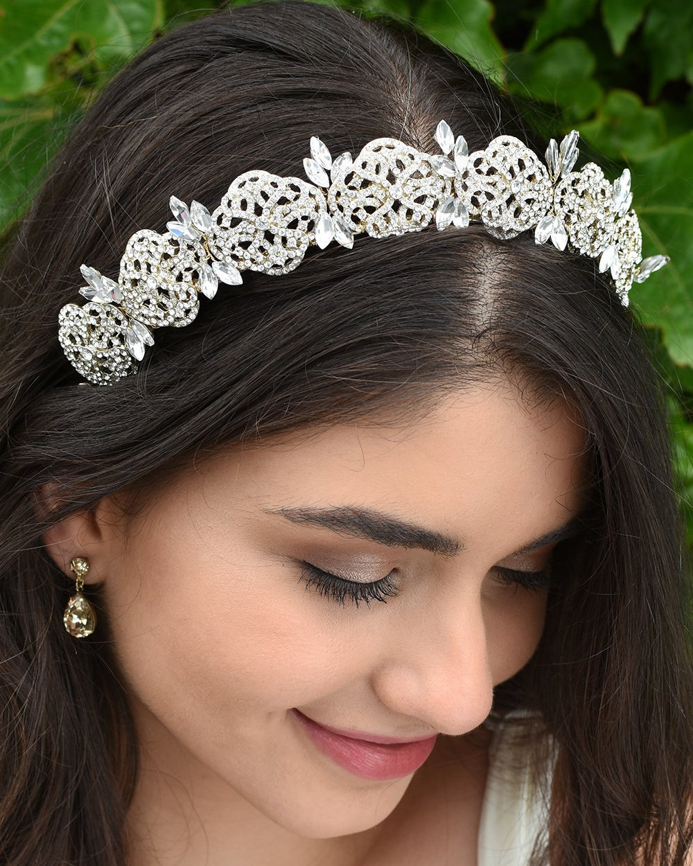 Smiling Bride looks down wearing a gold bridal headband full of tiny crystals with a background of leaves