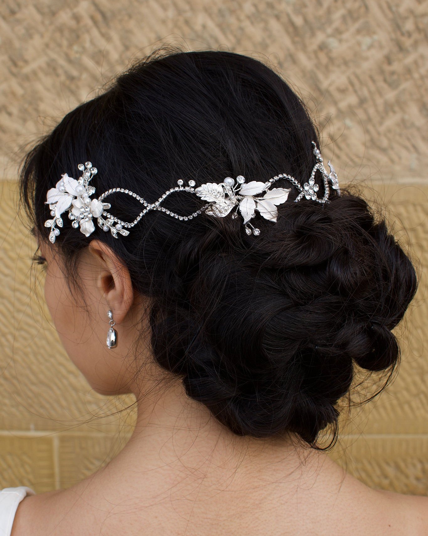 A dark haired model with curly hair wears a silver vine at the back of her head