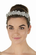 A woman with her hair styled in an updo wears an ornate silver filigree tiara against a plain white background.