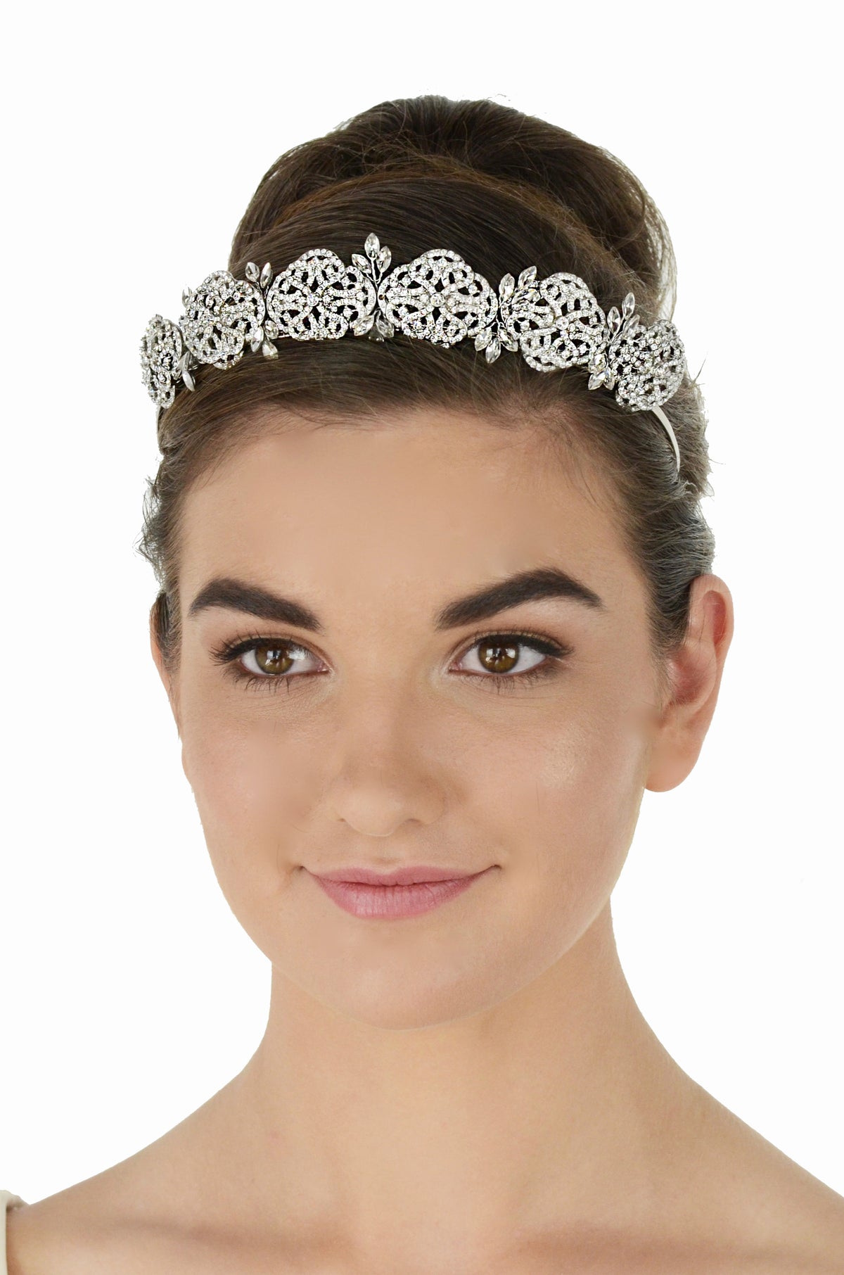 A woman with her hair styled in an updo wears an ornate silver filigree tiara against a plain white background.