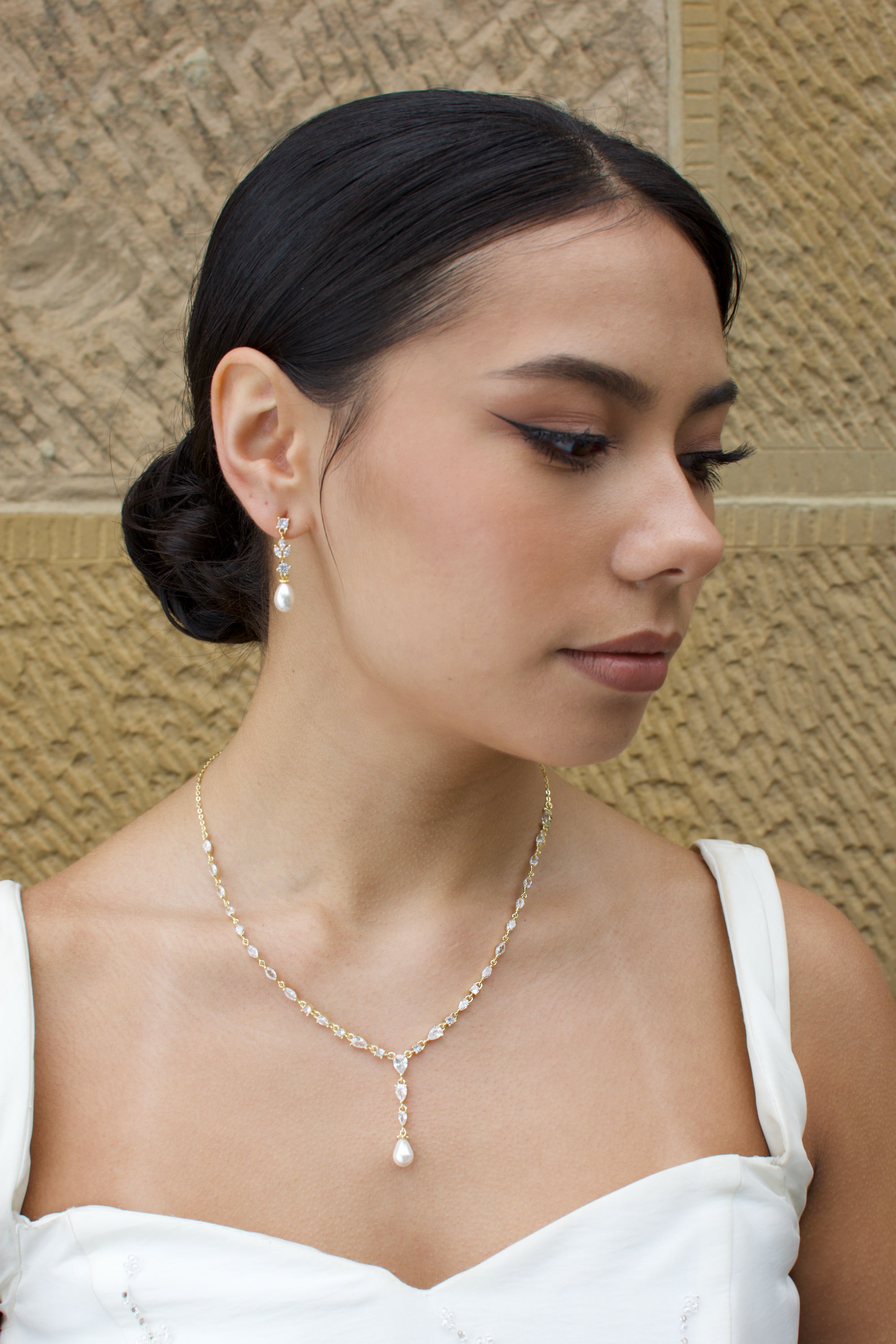 Woman wearing a pearl necklace and earrings against a textured wall.