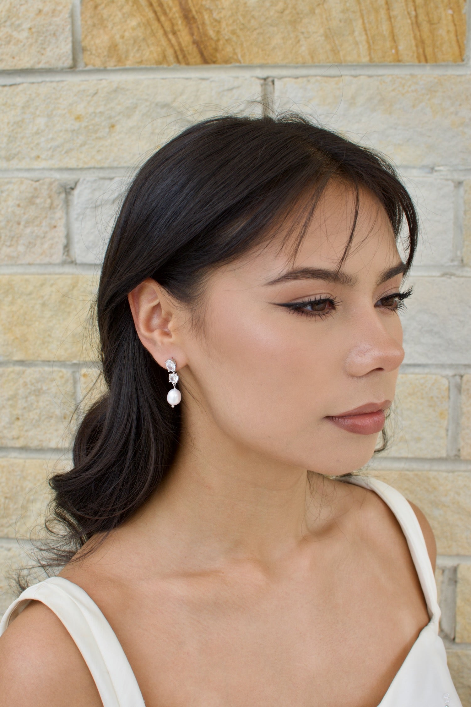 A woman wearing a white dress and earrings with real freshwater pearls and crystal stones.