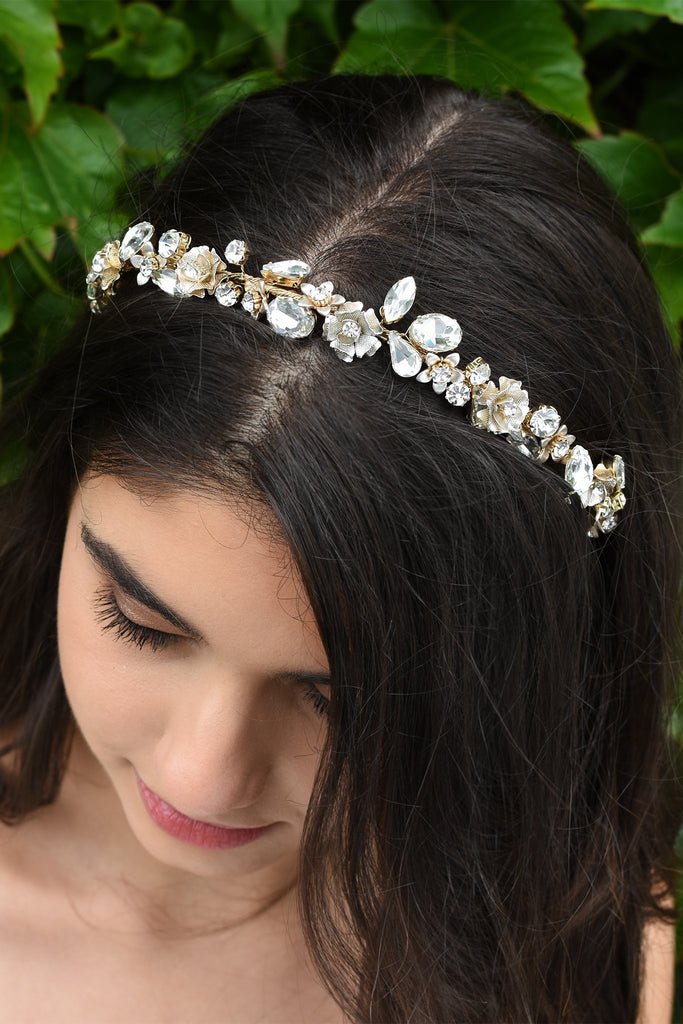 Dark hair smiling Bride wearing a thin headband full of different shapes of stones with green leaves in the background