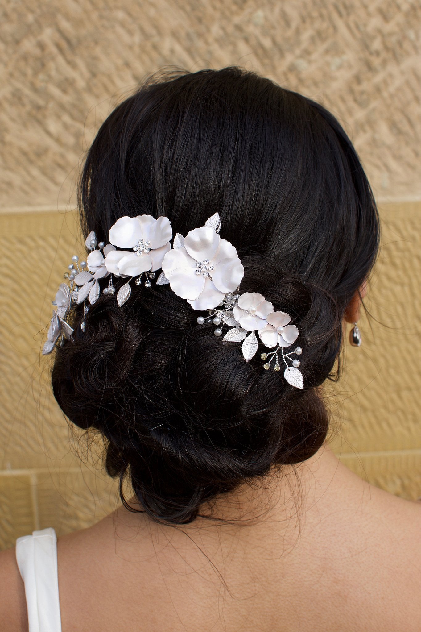 Black haired bride wears a white bridal clip in front of a sandstone wall