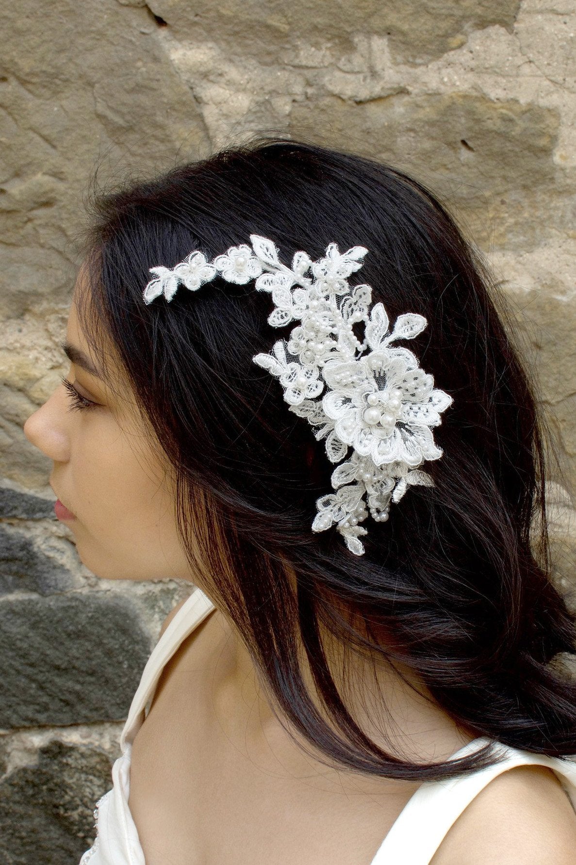 White lace bridal side comb with pearls worn by a bride in front of a stone wall