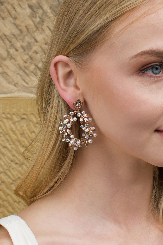 Model with blonde hair wears a rose gold hoop earring with pearls with a stone wall backdrop