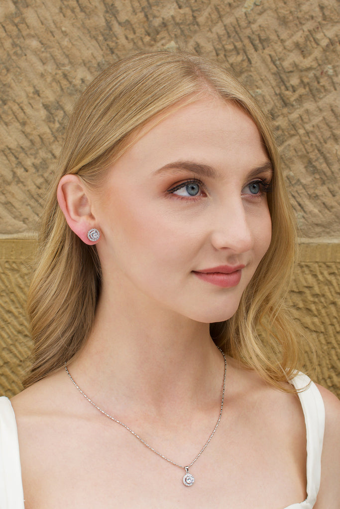 Model wears a silver chain pendant necklace with a single stone and a matching stud earring