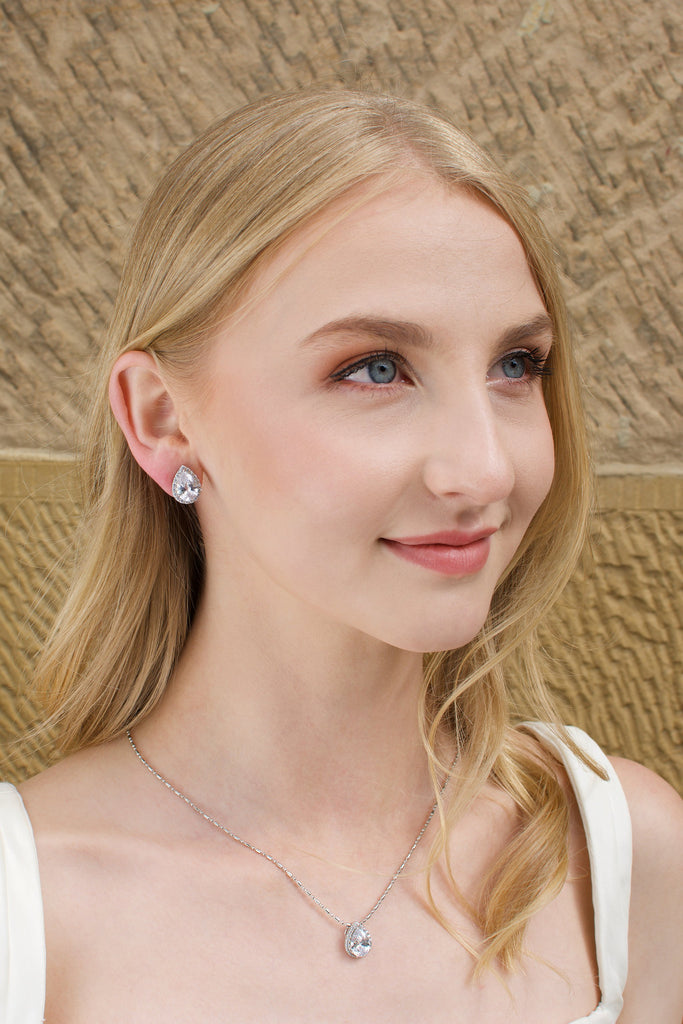Blonde model wears a crystal teardrop earring and necklace set. A Sandstone wall is the background