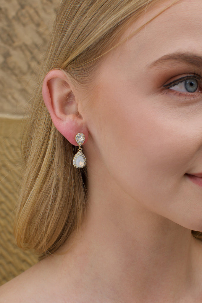 A blonde model wears a gold and white opal earring with a stone wall background