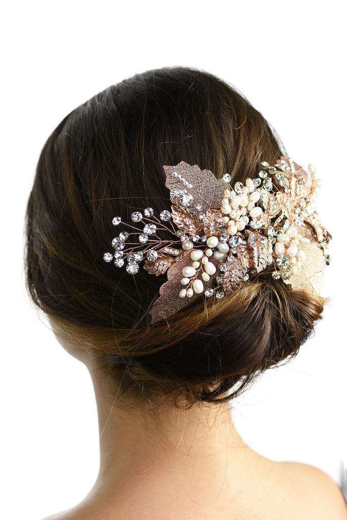 A model with brown hair wears a rose gold and filigree leaves Bridal Vine at the back of her head against a white background