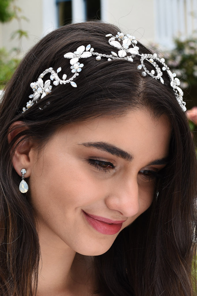 Dark Haired smiling model wears a silver bridal headband with white opal stones with a garden background