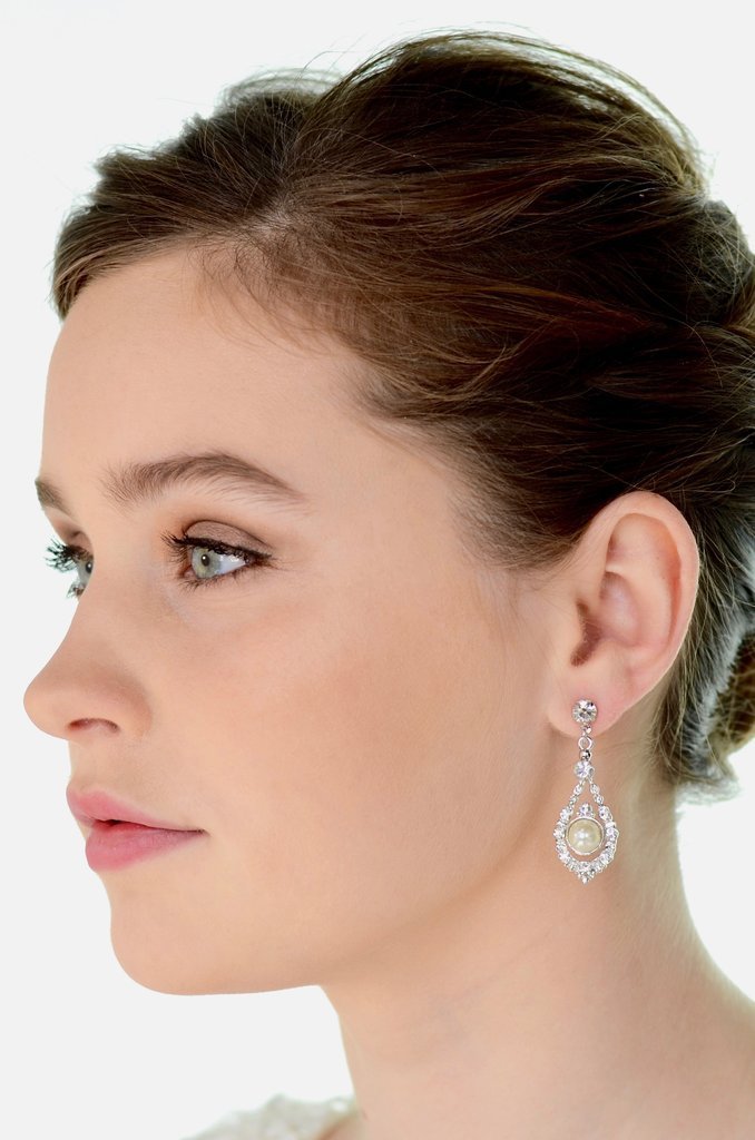 A green eyed model wears a pearl drop earring against a white background