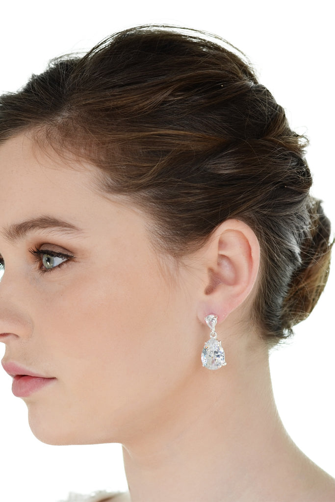 Dark haired model wearing a pear shaped stone earring against a white background. 