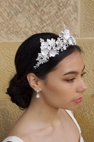 A dark haired bride wears a three pointed flower tiara at the front of her head. Behind is a sandstone wall.