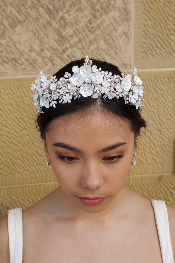 A Black  haired bride wears a three pointed silver flower tiara at the front of her head. Behind is a sandstone wall.