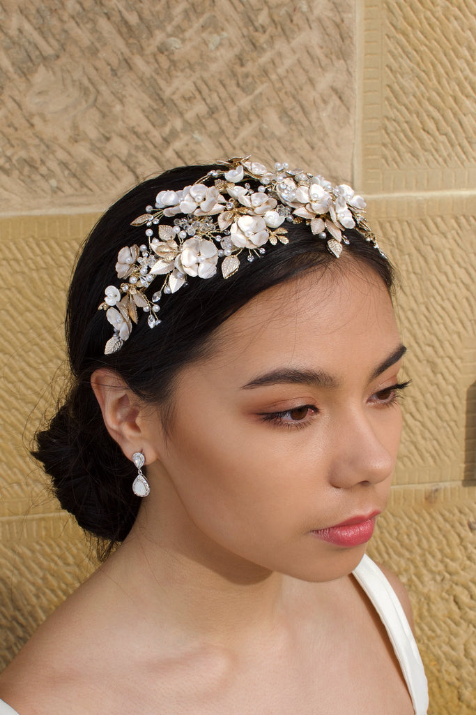 Dark Haired model wears a wide Pale Gold headband of flowers with the background of a stone wall