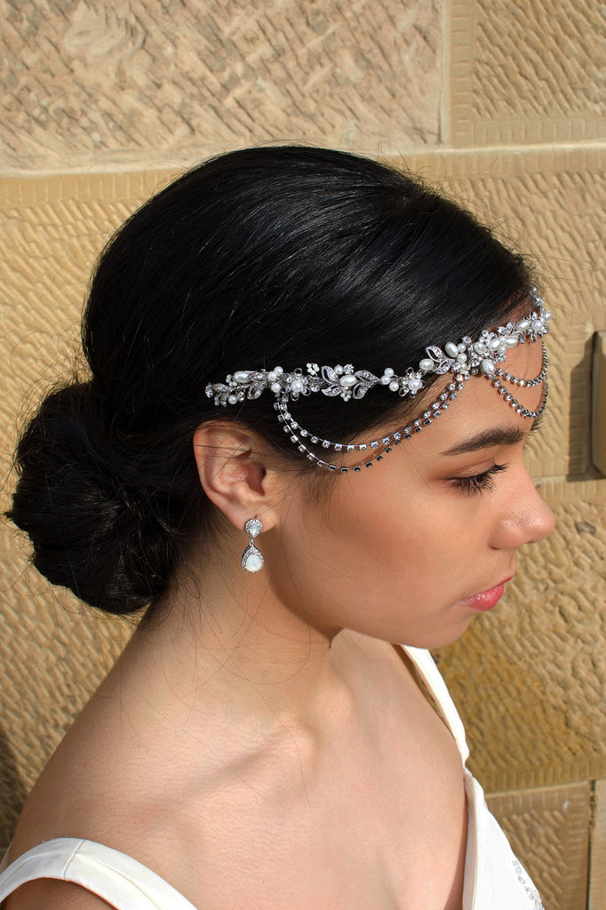 A side view of a bridal vine worn across the forehead of a dark hair bride. With a stone wall behind