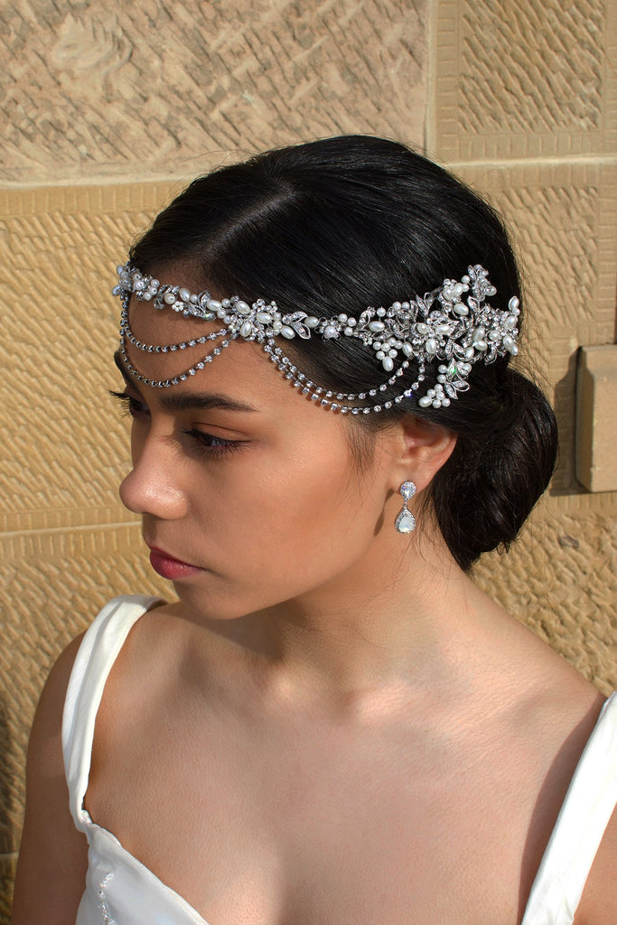 A black haired model wears a bridal vine with loops at the front of the head. With a stone wall background
